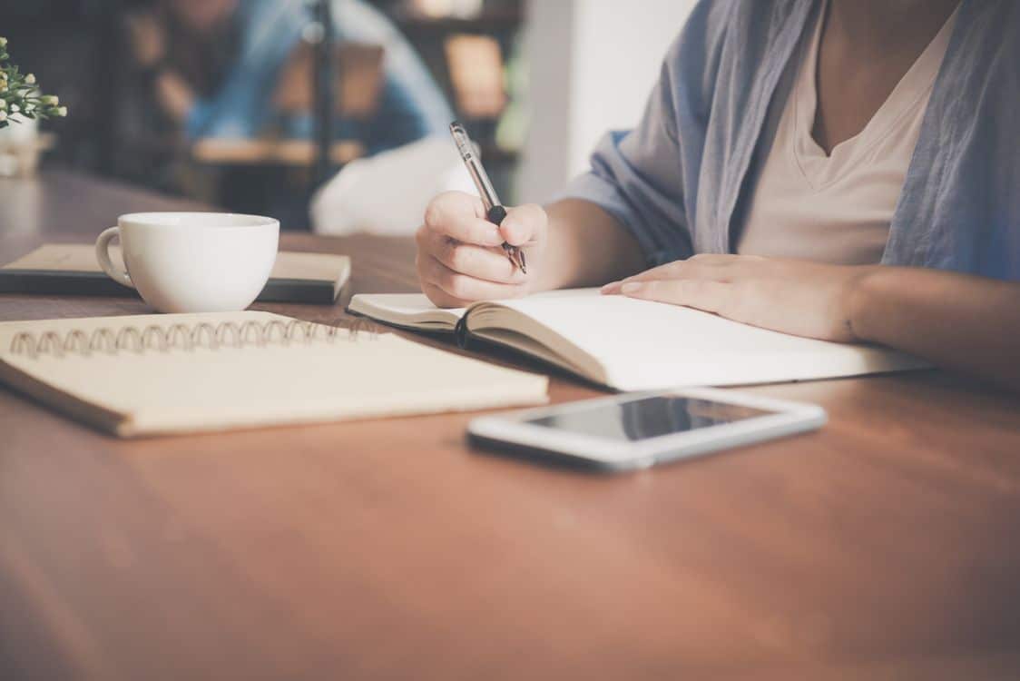 CAMS exam guide - Professional woman studying with notebook and coffee, preparing for the CAMS certification exam with focused concentration